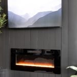 A modern living room showcases a DIY electric fireplace and TV wall. The sleek black fireplace with glowing embers sits below the mounted TV. Flanking these are a green potted plant and one with broad leaves, infusing a touch of nature into the contemporary design.